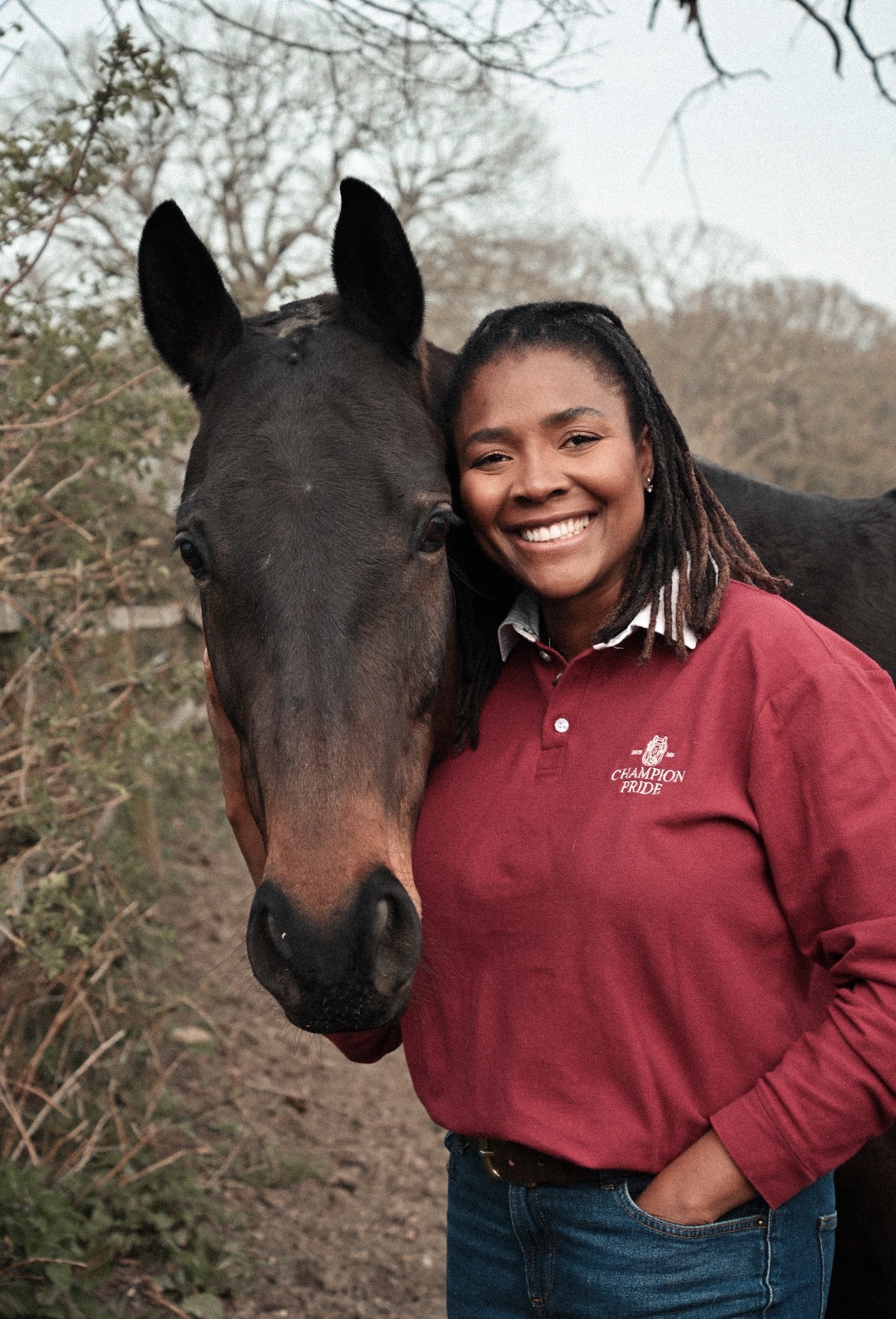 Zeze Oriaikhi-Sao smiling beside her horse in a burgundy Champion Pride rugby shirt